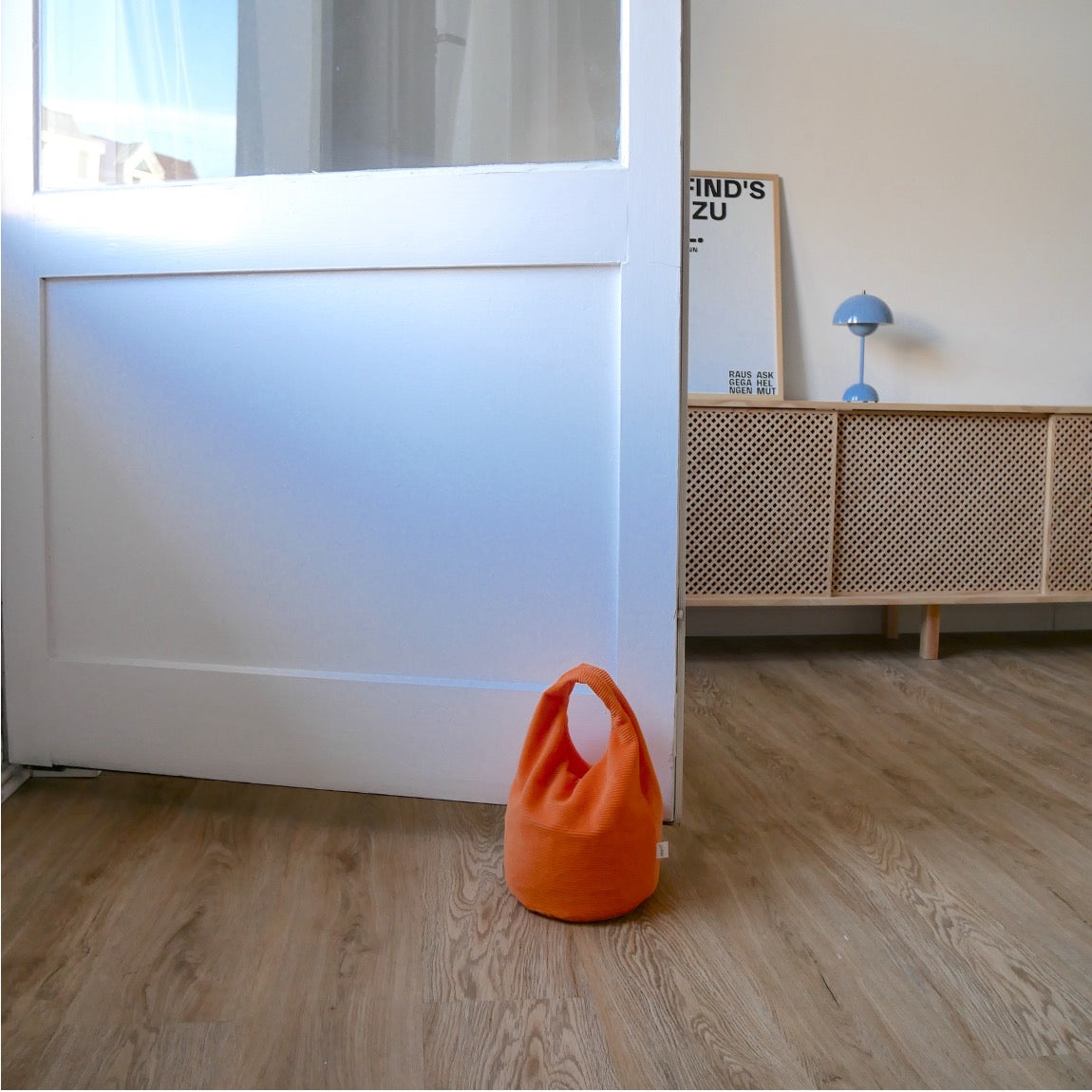 Türstopper Carrot Cordulino mit Baumwoll-Cordbezug von stop!t Produktfoto vor einer Balkontür demonstrierend die Tür vor Zugluft stoppend.