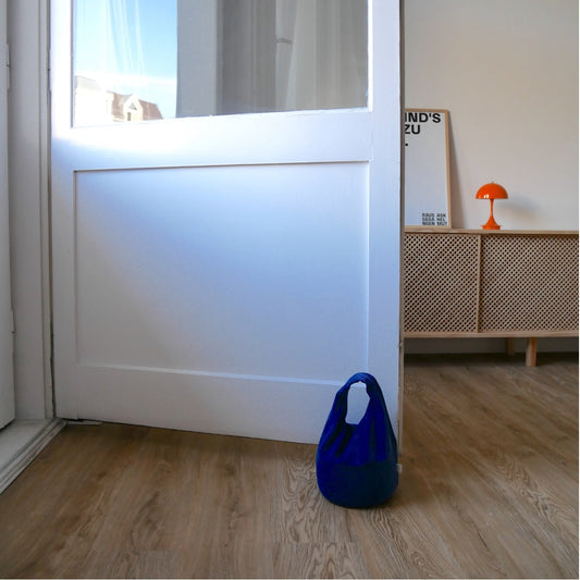 Türstopper Cobalt Cordulino mit Baumwoll-Cordbezug von stop!t Produktfoto vor einer Balkontür demonstrierend die Tür vor Zugluft stoppend.