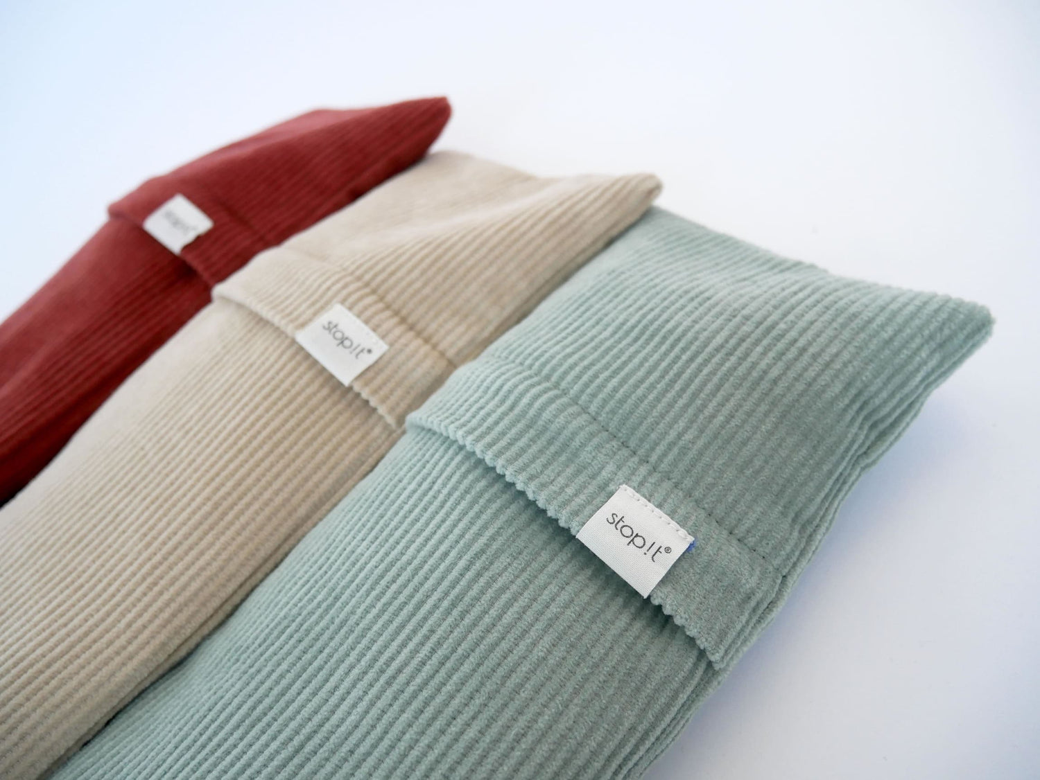 Drei Zugluftstopper aus Cordstoff liegen in Nahaufnahme schräg im Bild, bestehend aus den Farben: mint, beige und rostrot.