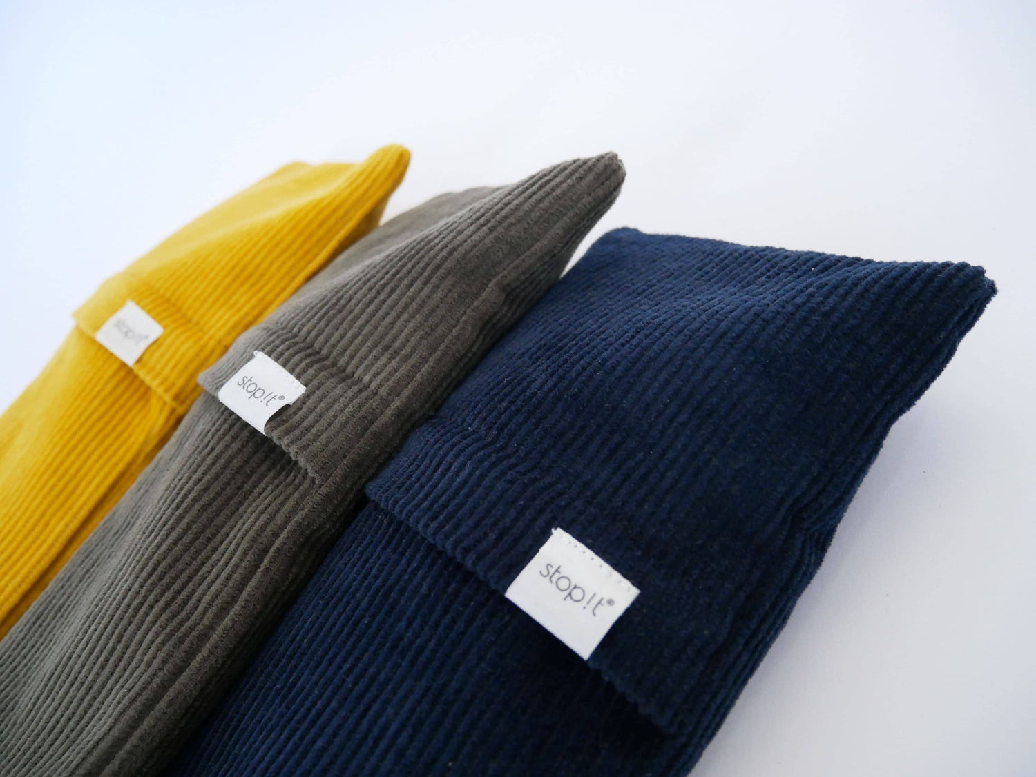 Drei Zugluftstopper aus Cordstoff liegen in Nahaufnahme schräg im Bild, bestehend aus den Farben: dunkelblau, olivgrün und gelb.