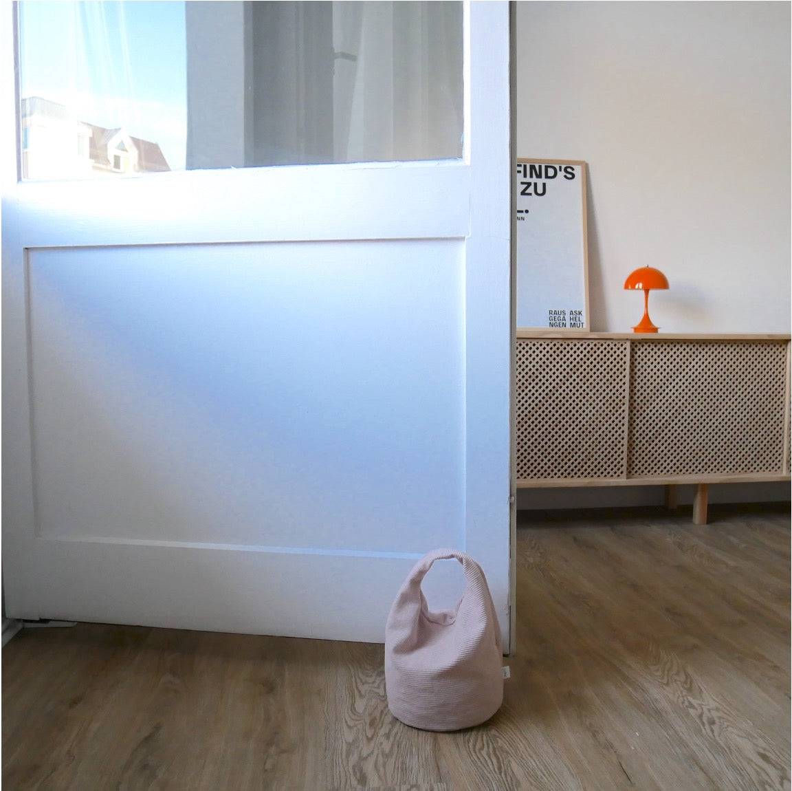 Türstopper Cotton Candy Cordulino mit Baumwoll-Cordbezug von stop!t Produktfoto vor einer Balkontür demonstrierend die Tür vor Zugluft stoppend.